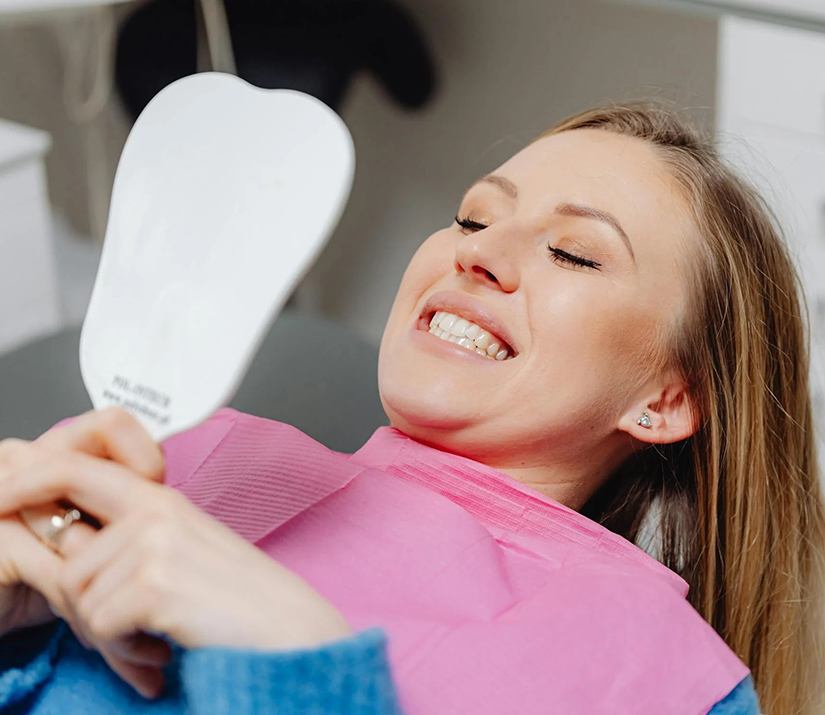 Woman in dentist’s chair looking in hand mirror