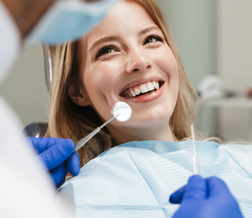 woman with blond hair in dental chair smiling with bib over her chest