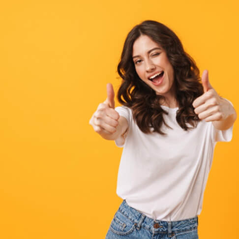 woman in white t-shirt and jeans giving two thumbs-up with yellow/orange background