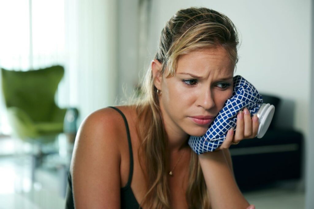 A woman holding an icepack to her jaw.